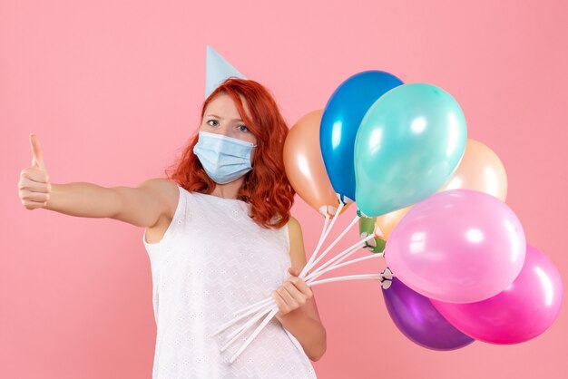 Vista frontal joven mujer sosteniendo globos de colores en máscara en la rosa