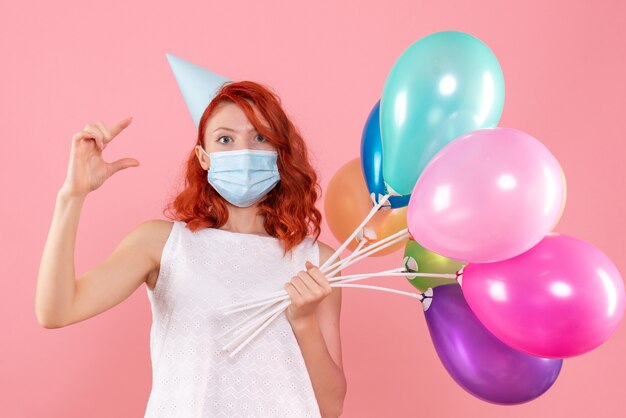 Vista frontal joven mujer sosteniendo globos de colores en máscara en la rosa