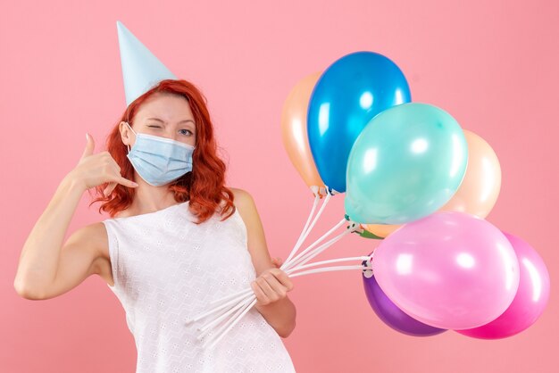 Vista frontal joven mujer sosteniendo globos de colores en máscara en la rosa