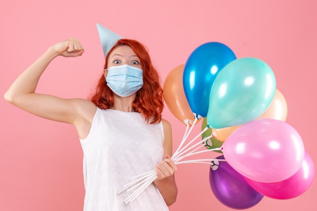 Vista frontal joven mujer sosteniendo globos de colores en máscara en la rosa