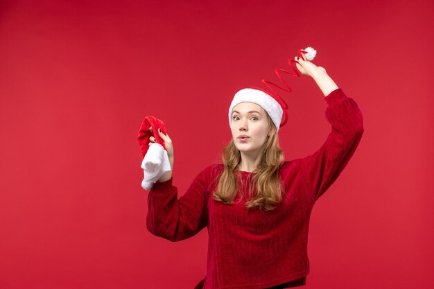 Vista frontal joven mujer sosteniendo gorra roja en el escritorio rojo Navidad vacaciones Navidad