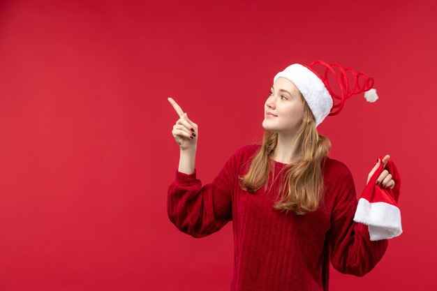 Vista frontal joven mujer sosteniendo gorra roja sobre escritorio rojo vacaciones navidad