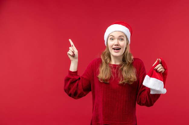 Vista frontal joven mujer sosteniendo gorro rojo sonriendo, vacaciones de Navidad