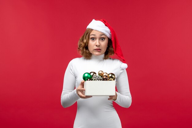 Vista frontal de la joven mujer sosteniendo juguetes de Navidad en rojo