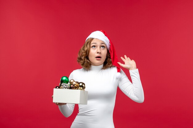 Vista frontal de la joven mujer sosteniendo juguetes de Navidad en rojo