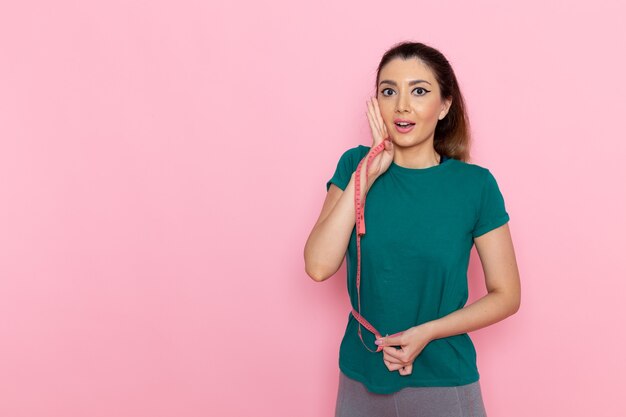 Vista frontal joven mujer sosteniendo la medida de la cintura en la pared rosa claro belleza deporte ejercicio atleta entrenamientos delgado