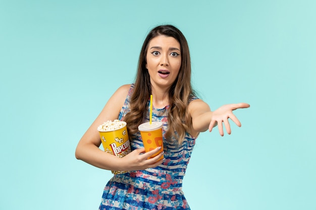 Vista frontal joven mujer sosteniendo palomitas de maíz y bebida en la superficie azul