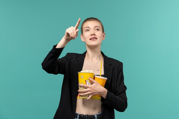 Vista frontal joven mujer sosteniendo palomitas de maíz con bebida y viendo películas en la superficie azul