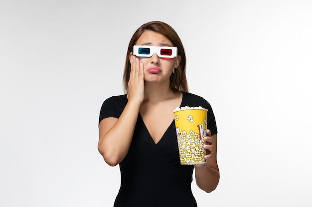 Vista frontal joven mujer sosteniendo palomitas de maíz en d gafas de sol viendo la película y llorando en la superficie blanca