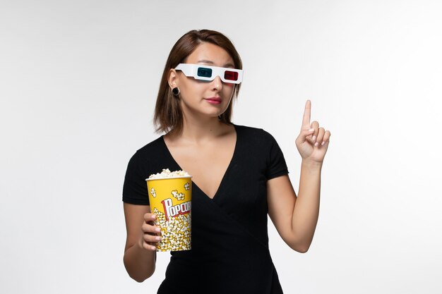 Vista frontal joven mujer sosteniendo palomitas de maíz en d gafas de sol viendo la película en la superficie blanca