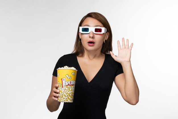 Vista frontal joven mujer sosteniendo palomitas de maíz en d gafas de sol viendo la película en la superficie blanca
