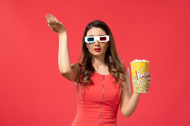 Vista frontal joven mujer sosteniendo palomitas de maíz en gafas de sol d en el escritorio rojo