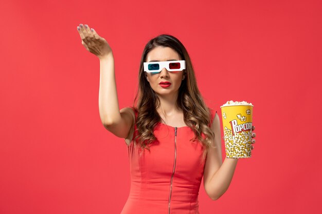 Vista frontal joven mujer sosteniendo palomitas de maíz en gafas de sol d en el escritorio rojo