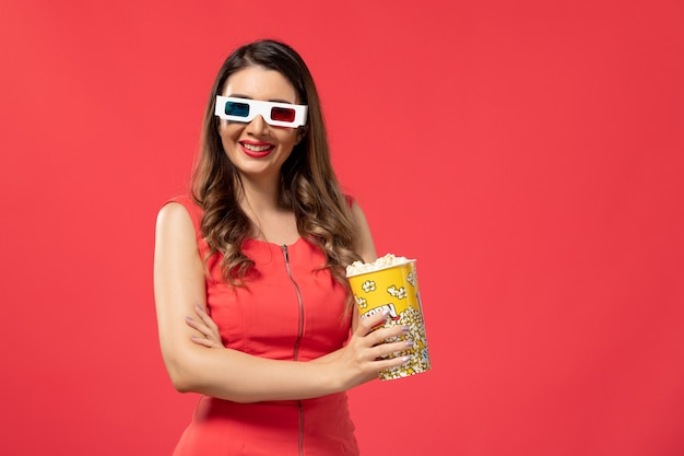 Vista frontal joven mujer sosteniendo palomitas de maíz en gafas de sol d en el escritorio rojo