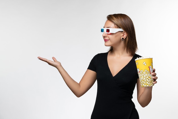 Vista frontal joven mujer sosteniendo palomitas de maíz en gafas de sol d sobre superficie blanca