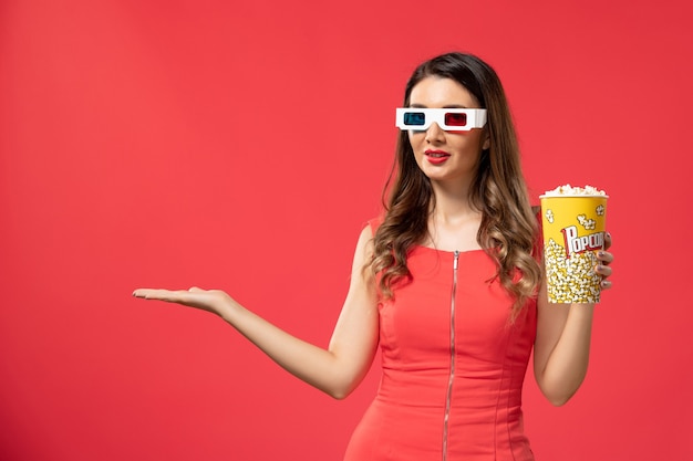 Vista frontal joven mujer sosteniendo palomitas de maíz en gafas de sol d sobre la superficie roja