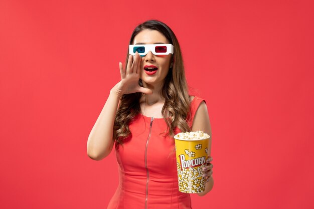 Vista frontal joven mujer sosteniendo palomitas de maíz en gafas de sol d sobre la superficie roja