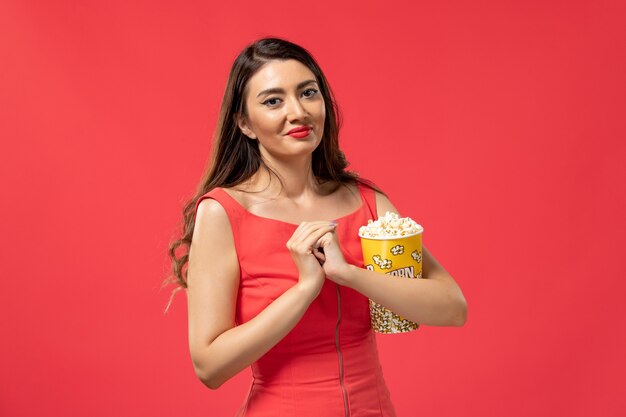Vista frontal joven mujer sosteniendo palomitas de maíz en la superficie roja