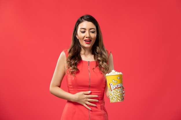 Vista frontal joven mujer sosteniendo palomitas de maíz en la superficie roja