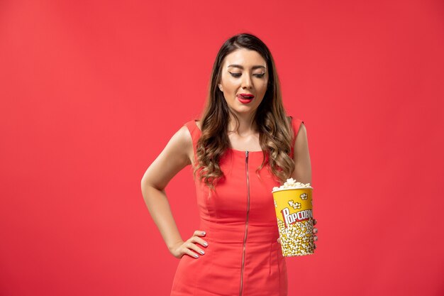 Vista frontal joven mujer sosteniendo palomitas de maíz en la superficie roja