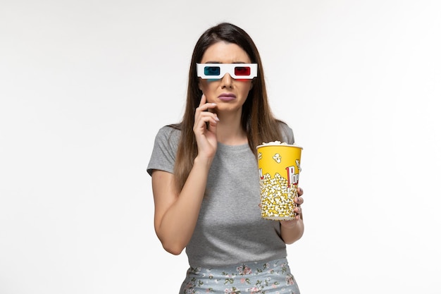 Vista frontal joven mujer sosteniendo palomitas de maíz y viendo películas en gafas de sol d sobre la superficie blanca clara