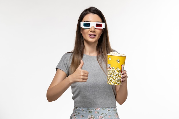 Vista frontal joven mujer sosteniendo palomitas de maíz y viendo películas en gafas de sol d sobre la superficie blanca clara