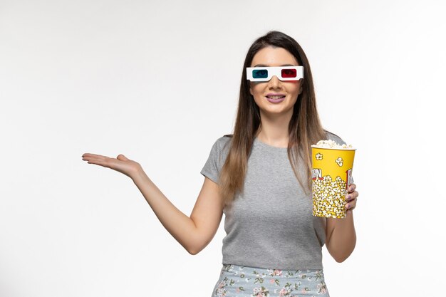 Vista frontal joven mujer sosteniendo palomitas de maíz y viendo películas en gafas de sol d sobre la superficie blanca clara