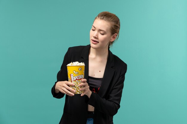 Vista frontal joven mujer sosteniendo palomitas de maíz y viendo películas en la superficie azul