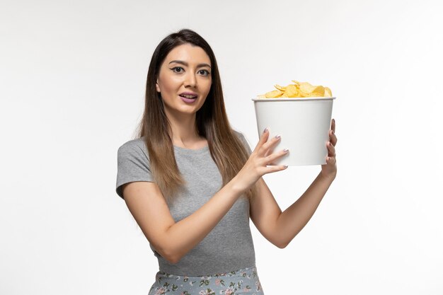 Vista frontal joven mujer sosteniendo papas fritas y viendo una película sobre una superficie blanca clara