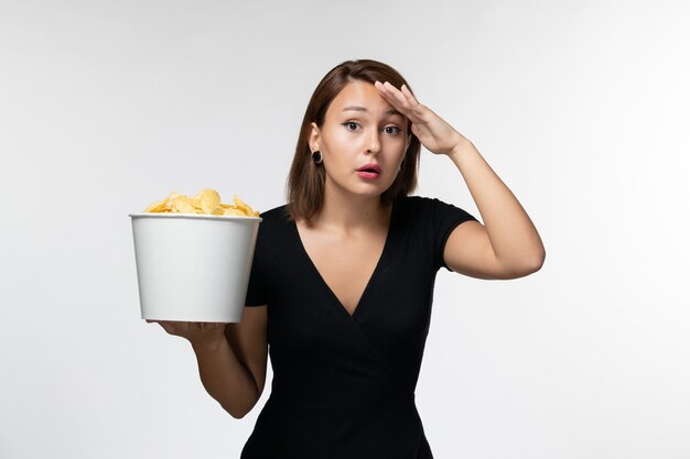 Vista frontal joven mujer sosteniendo papas fritas y viendo una película sobre una superficie blanca clara