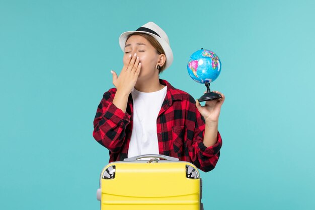 Vista frontal joven mujer sosteniendo un pequeño globo y preparándose para el viaje bostezando en el espacio azul