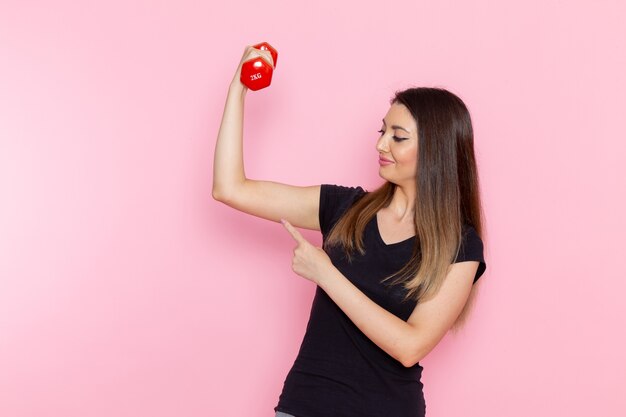 Vista frontal joven mujer sosteniendo pesas en el escritorio de color rosa claro atleta deporte ejercicio salud entrenamiento