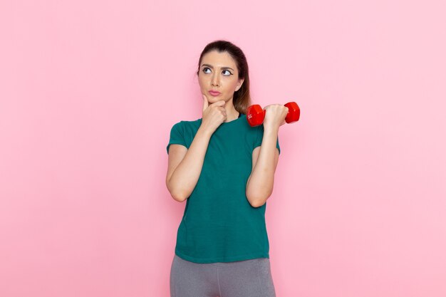 Vista frontal joven mujer sosteniendo pesas en la pared rosa atleta deporte ejercicio salud entrenamientos