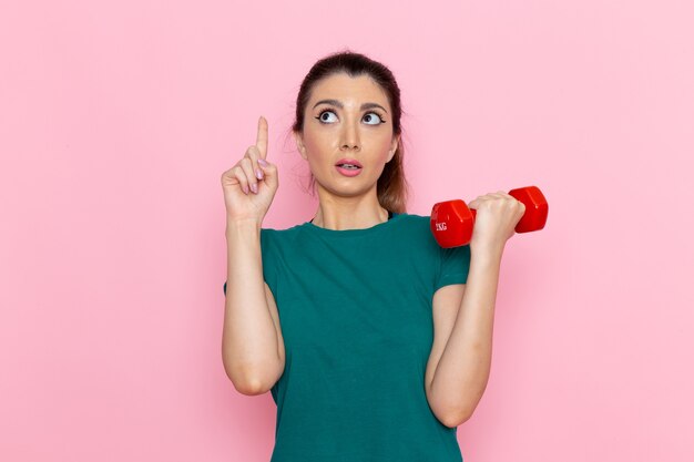 Vista frontal joven mujer sosteniendo pesas en la pared rosa atleta deporte ejercicio salud entrenamientos