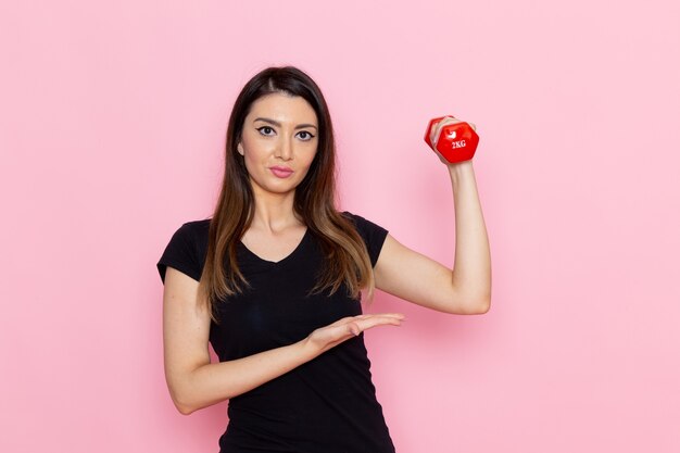 Vista frontal joven mujer sosteniendo pesas en la pared rosa claro atleta deporte ejercicio salud entrenamiento