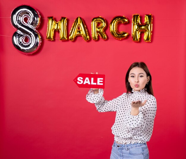 Vista frontal joven mujer sosteniendo placa de identificación de venta en marzo decorado fondo rojo compras amor cariñoso horizontal igualdad mujer vacaciones femenino