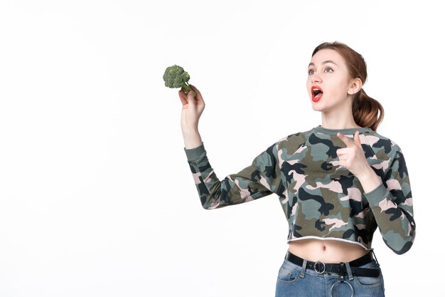 Vista frontal joven mujer sosteniendo poco brócoli verde sobre blanco