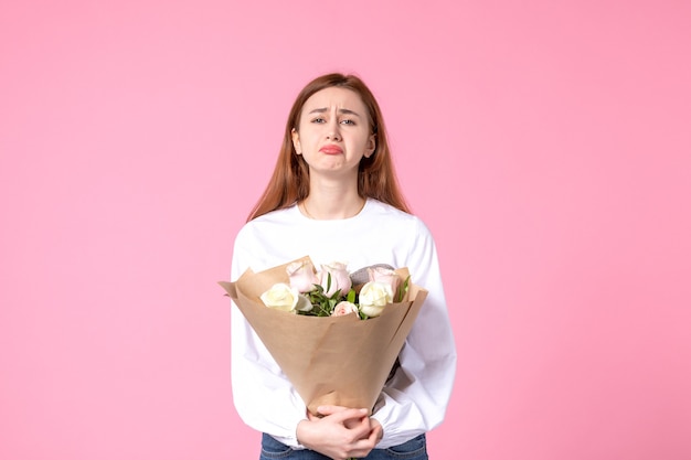 Vista frontal joven mujer sosteniendo ramo de rosas hermosas en rosa