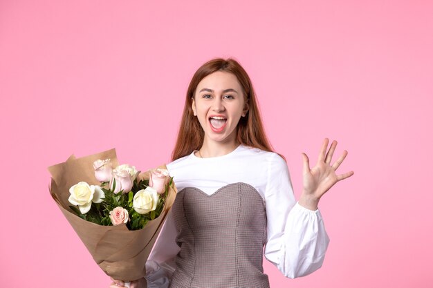 Vista frontal joven mujer sosteniendo ramo de rosas hermosas en rosa