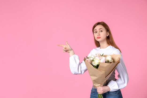 Vista frontal joven mujer sosteniendo ramo de rosas hermosas en rosa