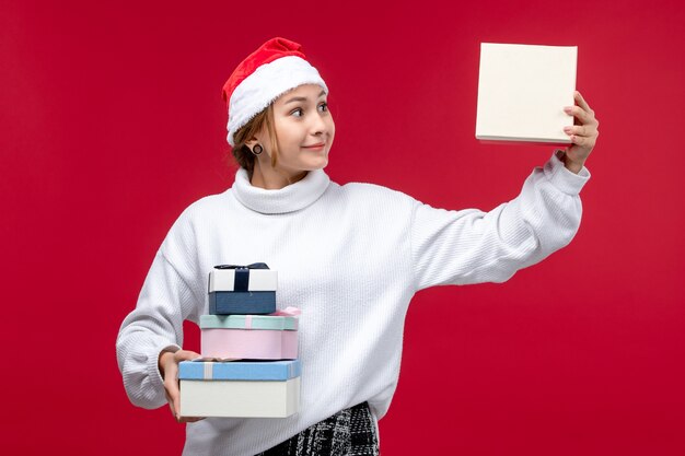 Vista frontal joven mujer sosteniendo regalos de año nuevo en rojo piso rojo Navidad vacaciones
