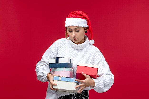 Vista frontal joven mujer sosteniendo regalos de año nuevo sobre fondo rojo claro