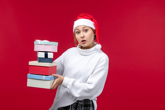 Vista frontal joven mujer sosteniendo regalos de año nuevo sobre fondo rojo claro