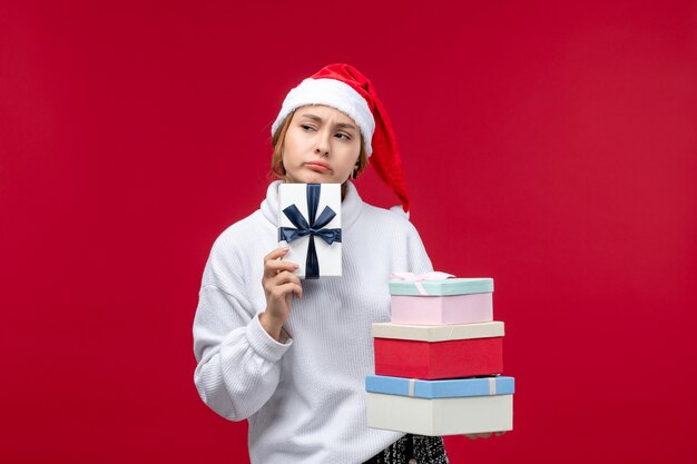 Vista frontal joven mujer sosteniendo regalos de año nuevo sobre fondo rojo.