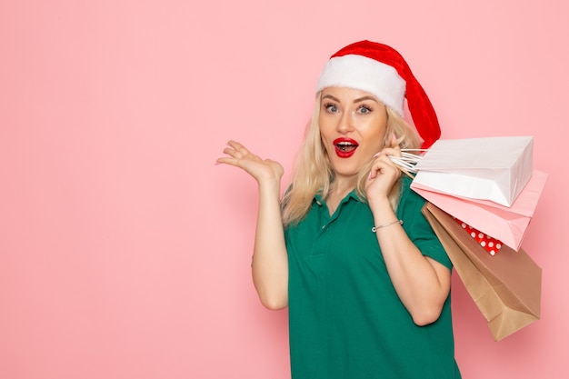 Vista frontal joven mujer sosteniendo regalos de navidad en paquetes en la pared rosa modelo vacaciones navidad año nuevo color de la foto
