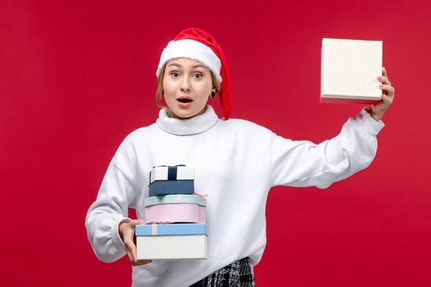 Vista frontal joven mujer sosteniendo regalos navideños en el escritorio rojo