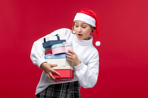 Vista frontal joven mujer sosteniendo regalos navideños en el escritorio rojo