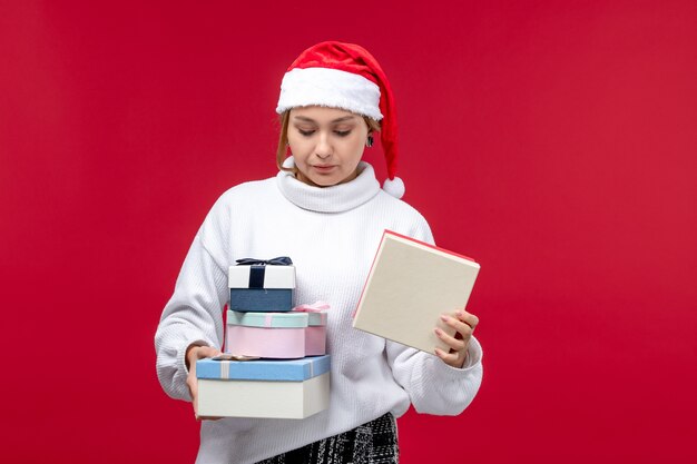 Vista frontal joven mujer sosteniendo regalos navideños sobre fondo rojo.