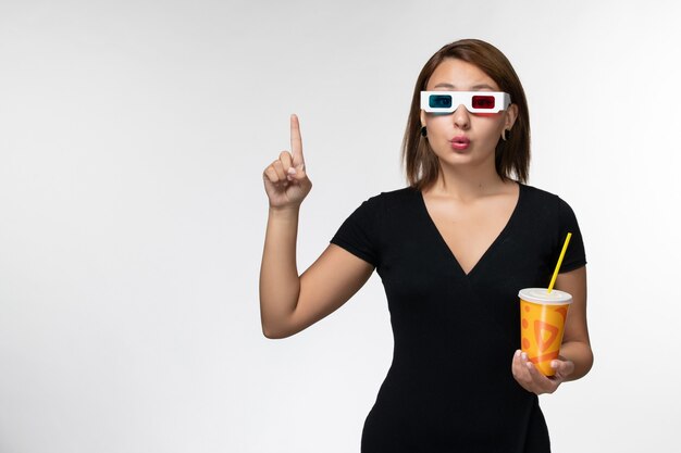 Vista frontal joven mujer sosteniendo soda en gafas de sol d sobre superficie blanca