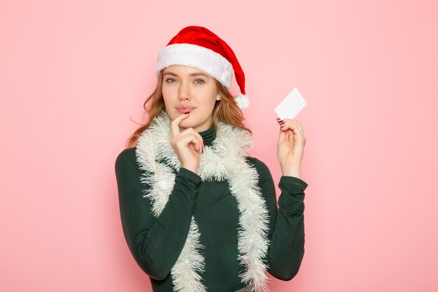 Vista frontal joven mujer sosteniendo una tarjeta bancaria blanca en la pared rosa color emoción modelo vacaciones navidad año nuevo